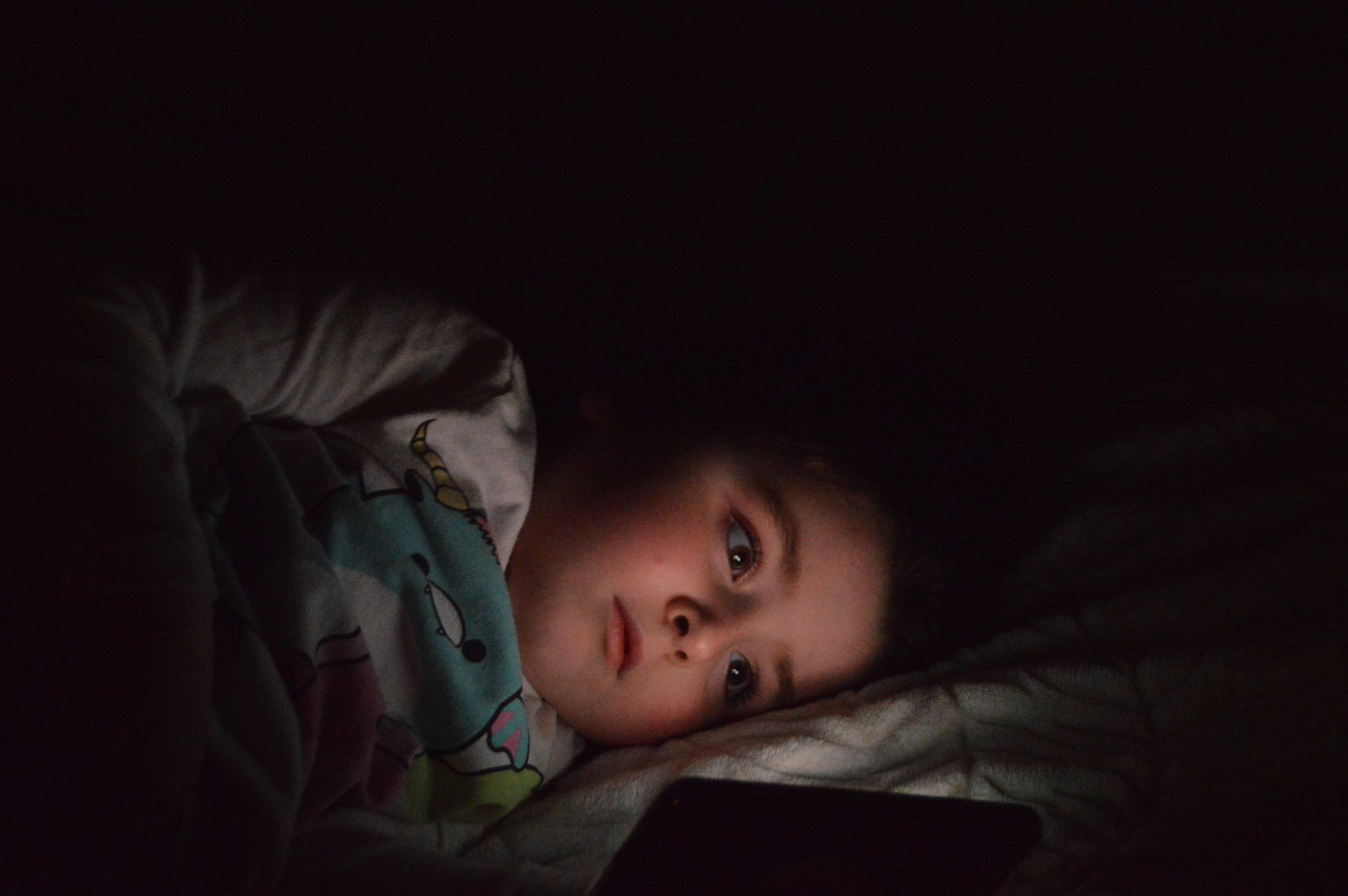 Low-light portrait of a child resting under a blanket
